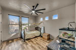 Bedroom with multiple windows, ceiling fan, light hardwood / wood-style floors, and a textured ceiling