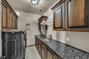 Laundry area with sink, light tile patterned floors, cabinets, a textured ceiling, and washer / clothes dryer