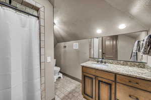 Bathroom featuring lofted ceiling, toilet, a textured ceiling, and vanity