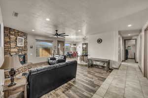 Living room with ceiling fan, a stone fireplace, light hardwood / wood-style floors, and a textured ceiling