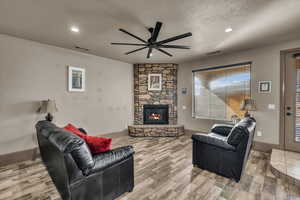 Living room featuring ceiling fan, a fireplace, hardwood / wood-style floors, and a textured ceiling