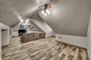 Bonus room featuring ceiling fan, vaulted ceiling, light hardwood / wood-style flooring, and a textured ceiling