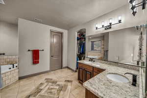 Bathroom with backsplash, vanity, tiled tub, tile patterned floors, and a textured ceiling