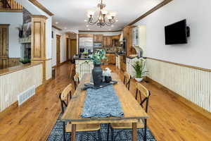 Dining room featuring a notable chandelier, ornamental molding, decorative columns, and light wood-type flooring