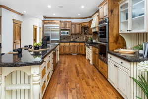 Kitchen featuring light wood-type flooring, appliances with stainless steel finishes, a kitchen breakfast bar, a large island, and decorative backsplash