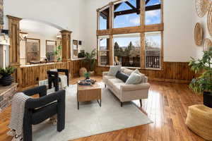 Living room featuring decorative columns, a towering ceiling, wooden walls, and light hardwood / wood-style flooring