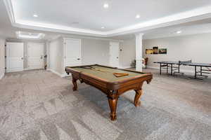 Recreation room featuring ornamental molding, a raised ceiling, light carpet, and ornate columns