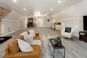 Carpeted living room featuring a fireplace, vaulted ceiling, sink, and ceiling fan