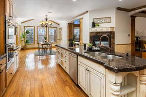 Kitchen with appliances with stainless steel finishes, sink, hanging light fixtures, light hardwood / wood-style floors, and a center island with sink