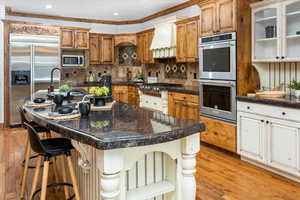 Kitchen featuring a breakfast bar, sink, a kitchen island with sink, stainless steel appliances, and custom range hood