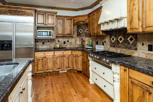 Kitchen with custom exhaust hood, crown molding, appliances with stainless steel finishes, and tasteful backsplash