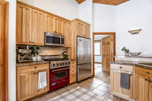 Kitchen with light tile patterned flooring, light brown cabinetry, stainless steel appliances, decorative backsplash, and a high ceiling