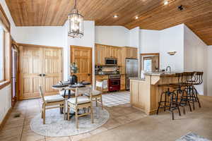 Dining room with light tile patterned flooring, a chandelier, high vaulted ceiling, and wooden ceiling