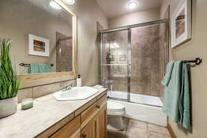 Full bathroom featuring vanity, toilet, tile patterned flooring, and combined bath / shower with glass door