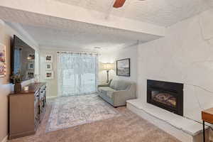 Living room with ceiling fan, light carpet, a textured ceiling, and a fireplace