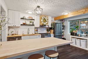 Kitchen with wood counters, sink, decorative light fixtures, stainless steel appliances, and white cabinets