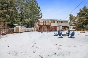 Snow covered house featuring a wooden deck, a shed, and a fire pit