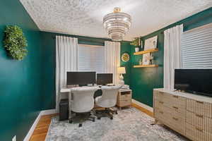 Home office featuring an inviting chandelier, light hardwood / wood-style floors, and a textured ceiling