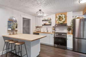 Kitchen with wood counters, hanging light fixtures, appliances with stainless steel finishes, a kitchen breakfast bar, and white cabinets