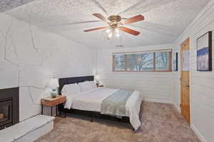 Bedroom with wood walls, light carpet, a textured ceiling, ceiling fan, and a fireplace