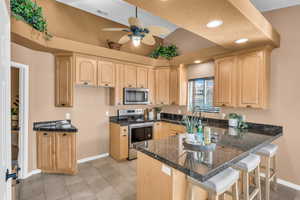 Kitchen with a breakfast bar, light brown cabinets, kitchen peninsula, and appliances with stainless steel finishes