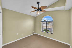 Empty room featuring ceiling fan, lofted ceiling, and carpet