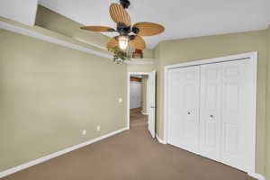 Unfurnished bedroom featuring a closet, ceiling fan, and dark colored carpet