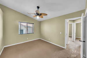 Carpeted spare room featuring vaulted ceiling, a textured ceiling, and ceiling fan