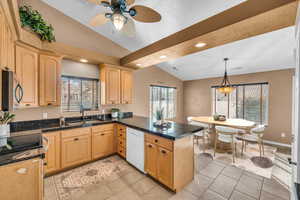 Kitchen featuring light brown cabinetry, dishwasher, vaulted ceiling, and kitchen peninsula