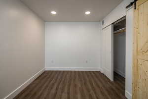 Unfurnished bedroom featuring dark hardwood / wood-style floors and a barn door