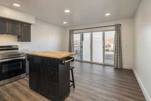 Kitchen featuring dark hardwood / wood-style floors, a breakfast bar, wooden counters, a center island, and stainless steel electric range