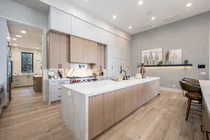 Kitchen with a large island, sink, light stone countertops, light hardwood / wood-style floors, and stainless steel gas stovetop