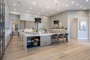 Kitchen with a large island, decorative light fixtures, light hardwood / wood-style floors, and white cabinets