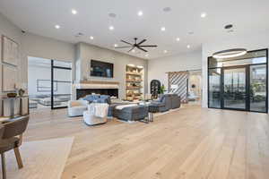 Living room with built in shelves, ceiling fan, a barn door, and light hardwood / wood-style floors