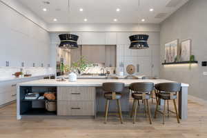 Kitchen featuring a breakfast bar area, backsplash, a large island with sink, hanging light fixtures, and light hardwood / wood-style flooring