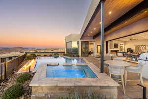 Pool at dusk with exterior fireplace, a patio area, a mountain view, and an in ground hot tub