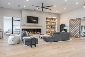 Living room with light hardwood / wood-style flooring, built in features, a barn door, and ceiling fan