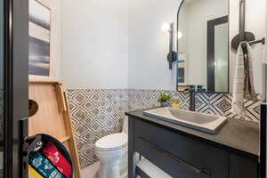 Bathroom featuring vanity, toilet, and tile walls