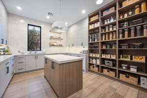 Interior space with hanging light fixtures, a center island, white cabinets, and light hardwood / wood-style flooring