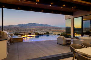 Pool at dusk with area for grilling, a mountain view, a patio, and an outdoor fire pit