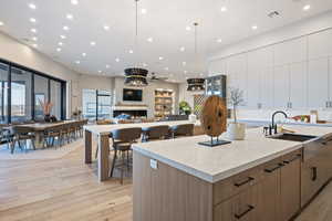 Kitchen with a spacious island, sink, hanging light fixtures, light stone countertops, and light hardwood / wood-style flooring