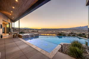 Pool at dusk with a mountain view, a patio area, and an in ground hot tub