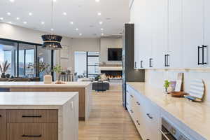 Kitchen featuring decorative backsplash, light stone countertops, white cabinets, and light hardwood / wood-style flooring