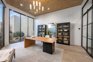 Office with plenty of natural light, a notable chandelier, light hardwood / wood-style floors, a barn door, and wooden ceiling