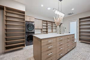 Walk in closet with light colored carpet and stacked washer and clothes dryer