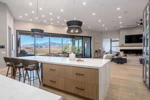 Kitchen with a spacious island, decorative light fixtures, light hardwood / wood-style flooring, a kitchen breakfast bar, and light stone countertops