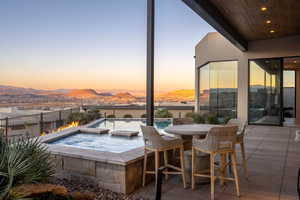 Pool at dusk featuring a bar, a mountain view, a patio, and an in ground hot tub