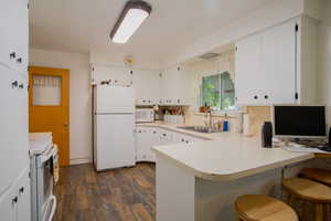 Kitchen featuring dark wood-type flooring, sink, white cabinetry, kitchen peninsula, and white appliances