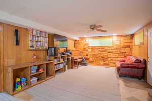 Living room with ceiling fan and wood walls