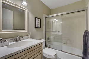 Full bathroom featuring vanity, combined bath / shower with glass door, and toilet